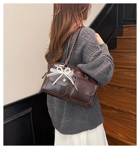 Detail of dark brown glossy leather underarm bag with lace bow and pearl charm