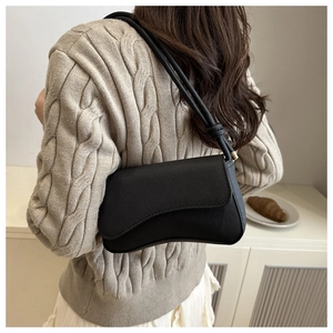 Detail of black textured leather shoulder bag with gold hardware on a model in knitwear