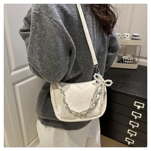 Détail du sac à bandoulière beige avec chaîne argentée et nœud en perles sur modèle