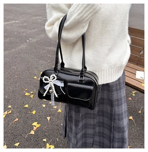 Détail du sac à bandoulière en cuir PU noir avec breloque nœud perle sur fond d'automne
