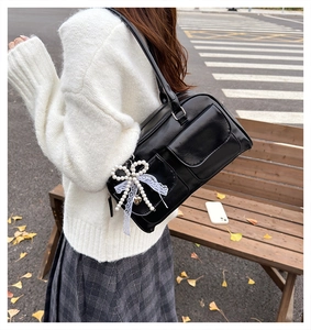 Detail of black faux leather underarm bag with pearl bow charm and dual front pockets