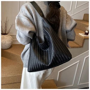 Detailed view of black woven hobo bag with wide shoulder strap on a model's shoulder