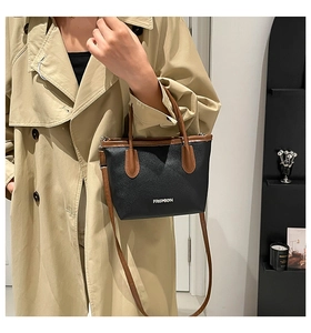 Minimalist black pebbled leather bucket bag with brown handles on khaki trench coat