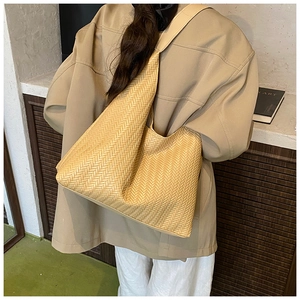 Detailed V-weave texture of a large khaki woven tote bag worn on a model's shoulder