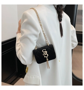 Détail du sac en velours noir avec matelassage, chaîne dorée et pendentif pompon en S