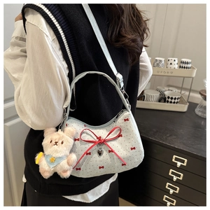 Détail d'un sac bandoulière bleu clair avec nœuds rouges et breloque ours en peluche