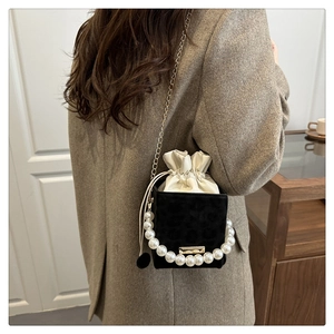 Detail of black mini bucket bag with large pearl handle and gold chain on wool coat
