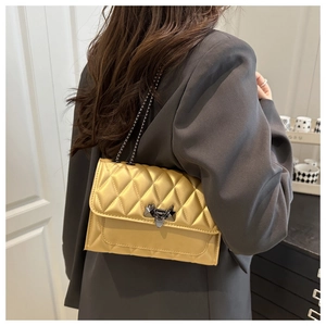 Close-up of mustard yellow quilted crossbody bag with dark grey metal chain and lock