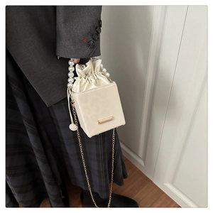 Detail of beige bucket bag featuring pearl handle and gold chain strap on a model