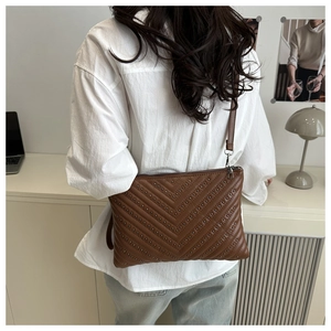 Rear view of model wearing a brown crossbody bag with metal studs and V-shaped quilting