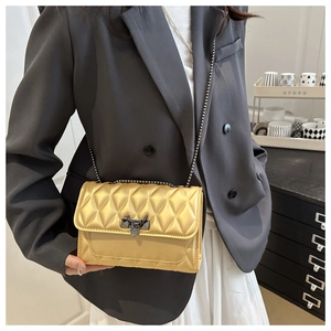 Close-up of gold quilted crossbody bag with metallic lock and dark chain strap