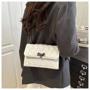 Close-up of a white quilted crossbody bag with a metal chain and clasp on a model