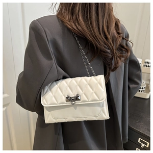 Detail of a beige quilted crossbody bag with gunmetal chain and heart stud clasp
