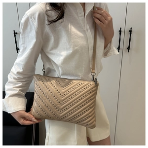 Dettaglio borsa a busta beige trapuntata a V con borchie in metallo indossata da modella