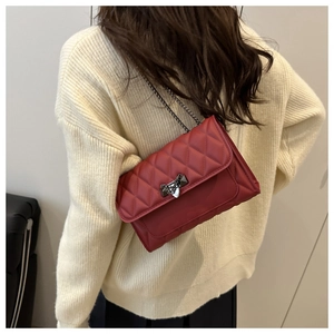 Close-up of a red quilted chain bag featuring a gold metal lock on a textured crossbody strap