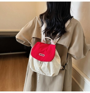 Detail of a mini nylon backpack with red flap and drawstring closure worn by a model