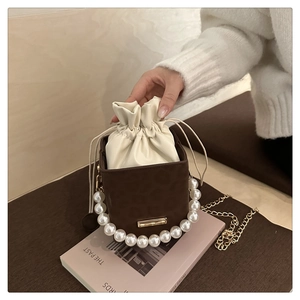 Detail of a brown suede pearl handle bucket bag with cream drawstring and gold chain