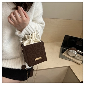 Close-up of leopard print bucket bag with pearl handle and golden chain strap on a desk
