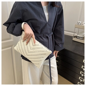 Close-up of white V-quilted handbag with black rivets held by a model in a cozy setting