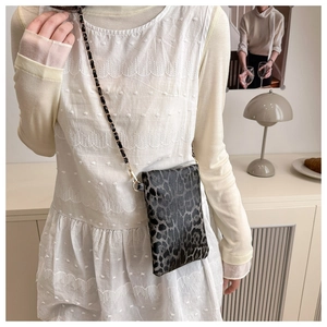 Close-up of a mini crossbody bag with grey leopard pattern and chain strap on a model