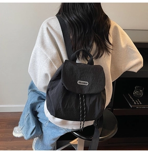 Rear view of model wearing black nylon backpack with flap closure and drawstring detail
