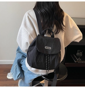 Detail of black nylon backpack with silver brand logo and drawstring closure in use