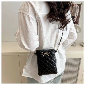Detail of black quilted crossbody bag with golden bow buckle and chain leather strap