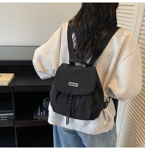 Detail of black nylon backpack featuring drawstring closure and silver brand nameplate