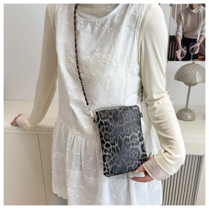 Detail of leopard print crossbody phone bag with metal and leather chain strap shown in use