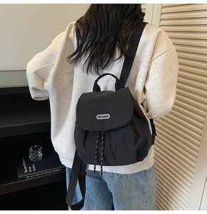 Detailed back view of a woman wearing a compact black nylon backpack with adjustable straps