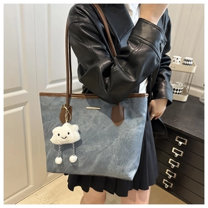 Blue canvas tote bag with brown leather trim and white cloud charm shown on shoulder