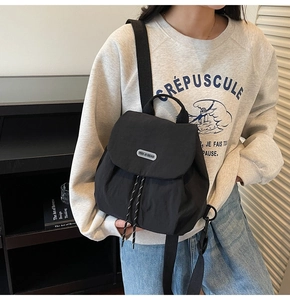 Lifestyle shot of woman wearing a black nylon backpack with flap and drawstring closure