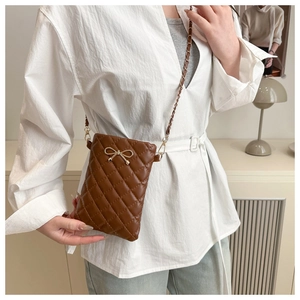 Brown quilted crossbody bag with gold bow ornament and chain strap shown on model