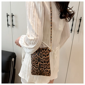 Detail of leopard print mini crossbody bag featuring a metal chain strap on white dress