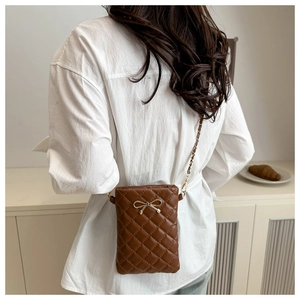 Détail du sac à bandoulière matelassé marron avec nœud doré et chaîne sur le modèle