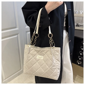Detail of beige quilted tote bag with gold chain strap and textured fabric finish