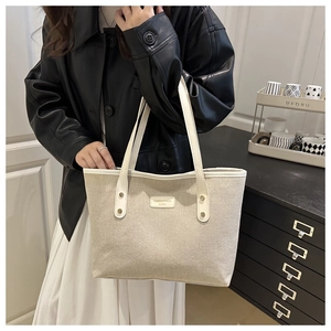 Detail of beige canvas tote bag with white leather straps and front logo patch