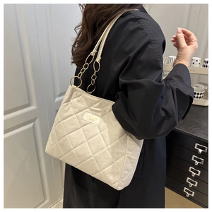 Detailed close-up of beige quilted tote bag featuring gold chain strap and metal nameplate