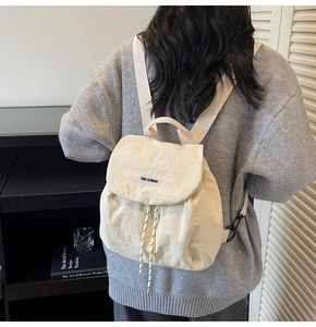 Close-up of cream nylon backpack featuring drawstring closure and top handle strap detail