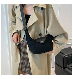 Close-up of black crescent hobo bag with silver buckle and wide strap on beige trench coat
