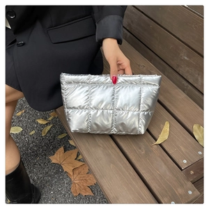 Trousse de maquillage matelassée argentée tenue par un mannequin, effet métallique