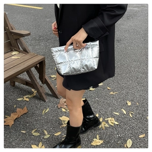Silver metallic quilted clutch bag held by model against an urban street background