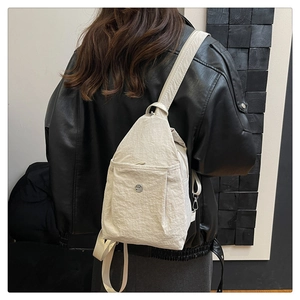 Detail of light beige nylon sling bag showing durable fabric and round metal logo detail