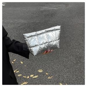 Close-up of a silver quilted clutch bag with metallic texture against a street background