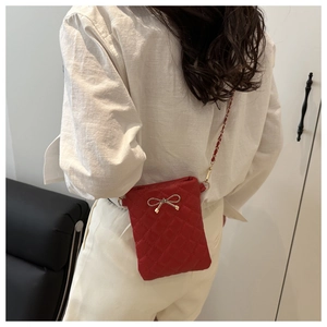 Détail d'un petit sac bandoulière matelassé rouge avec nœud doré et fine chaîne