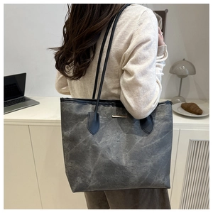Detail of large grey tote bag with stone texture and gold metal bar on white background