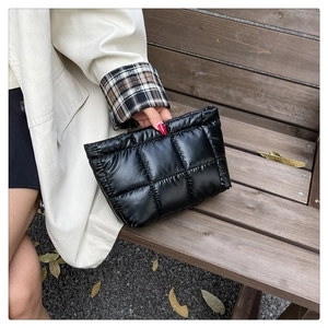 Close-up of a black quilted puffer clutch bag with glossy finish on a wooden bench outdoors