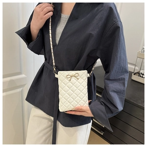 Détail d'un sac bandoulière blanc matelassé avec nœud doré et bandoulière chaîne