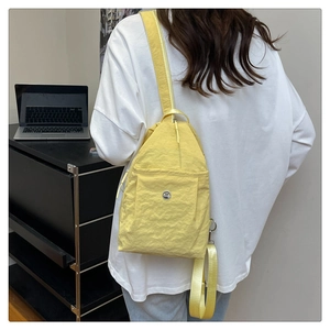 Detail of bright yellow crinkled nylon sling bag featuring circular metal logo and strap