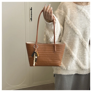 Detail of woven brown tote bag with leather straps and decorative wooden beads